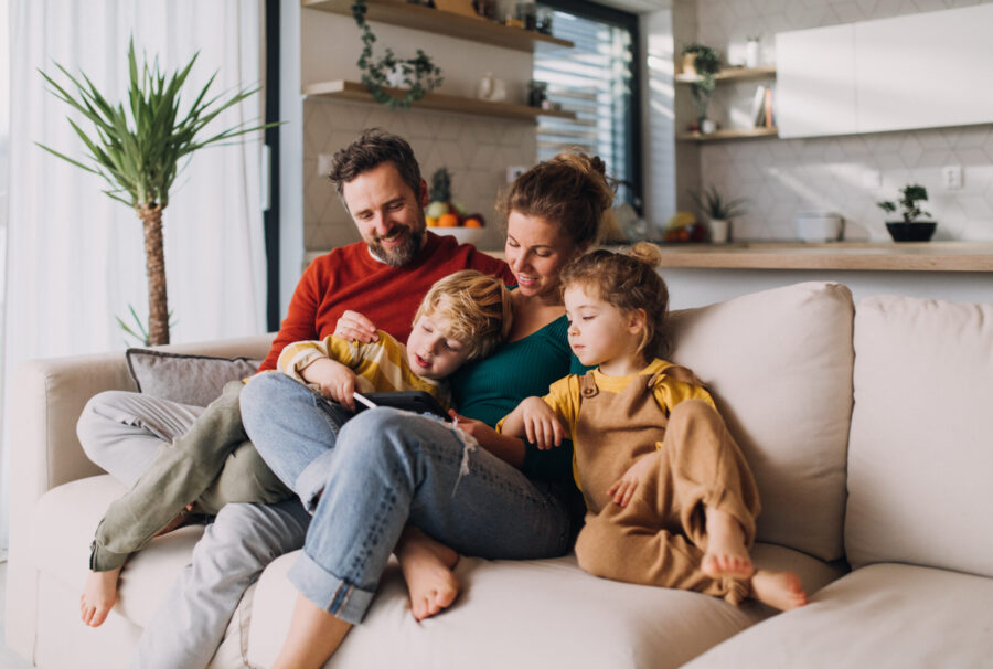 Little children bonding with parents on sofa at home and using tablet.