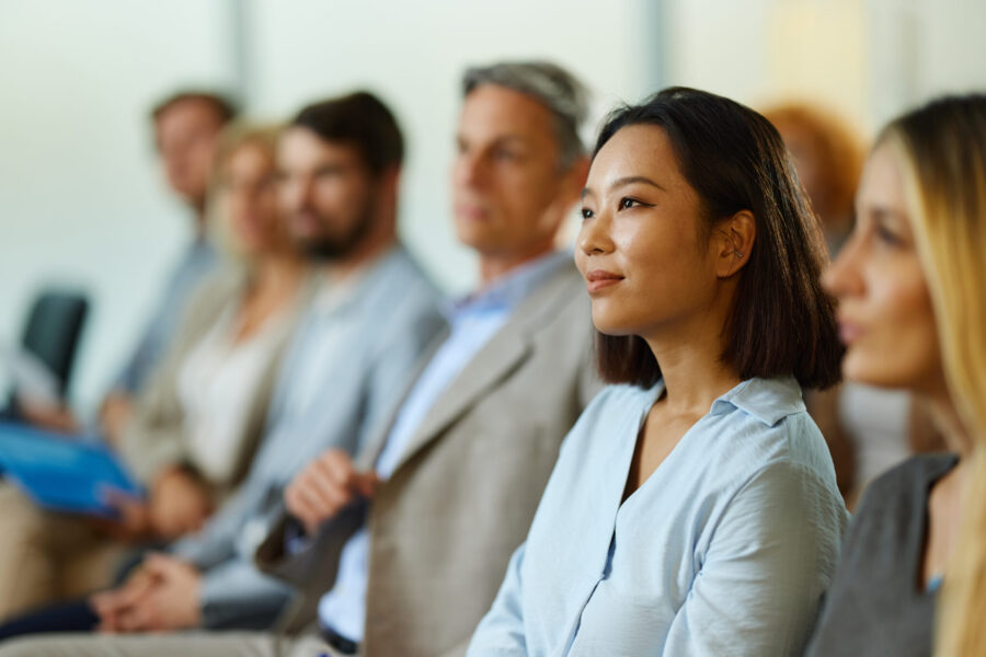 Young smiling Chinese businesswoman and her colleagues attending an education event in the office.