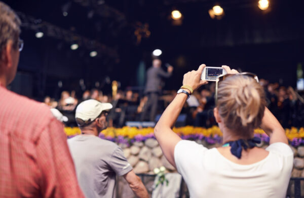 Rearview shot of a woman in the crowd holding a camera to photograph the concert
