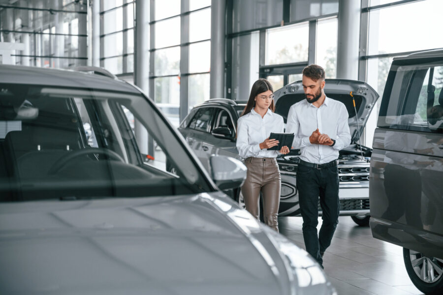 Walking Forward And Talking. Man With Woman In White Clothes Are In The Car Dealership Together