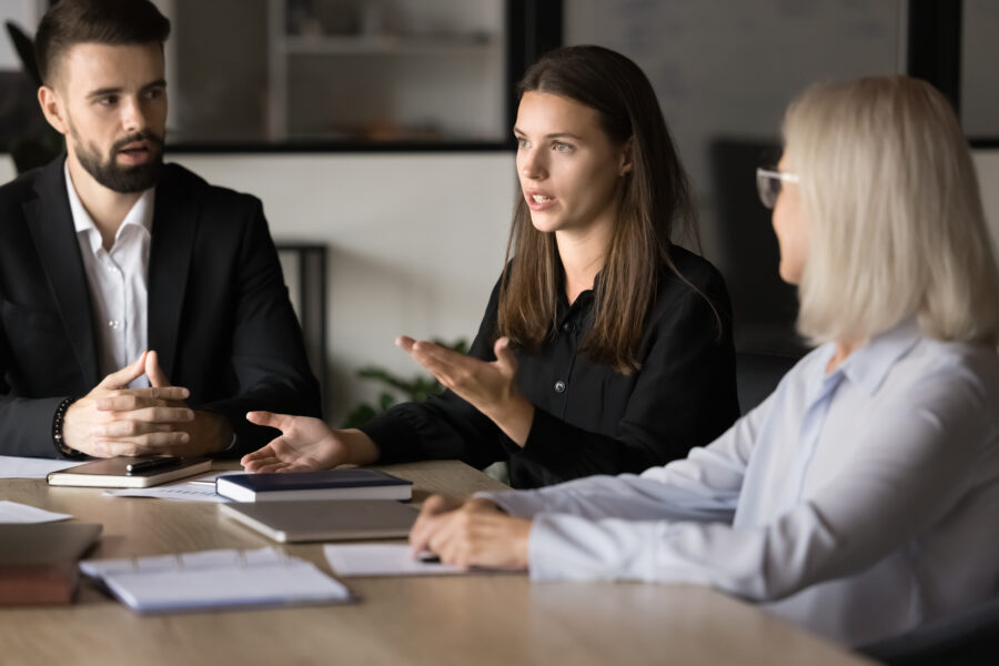 Serious pretty young project manager talking to coworkers on brainstorming meeting, offering management strategy, work ideas for project, speaking to boss and colleagues