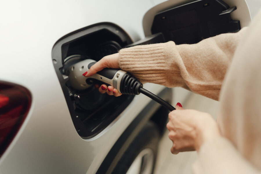 Close-up of young woman charging her electric car in autumn day.