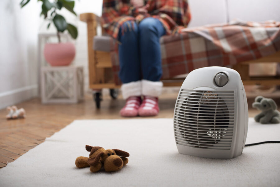 Electric fan heater on the floor in living room with human sitting on the sofa at background