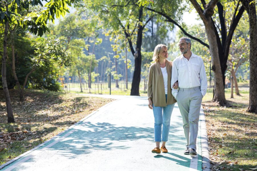 Senior citizen couple taking a walking in a park during summer morning. Seniors couple spend time in public park together.