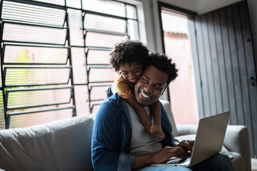 Father using the laptop while son is on his back at home