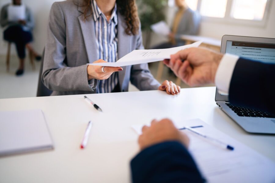 In the office young Caucasian female candidate, giving her CV or application form to male recruiter during a job interview