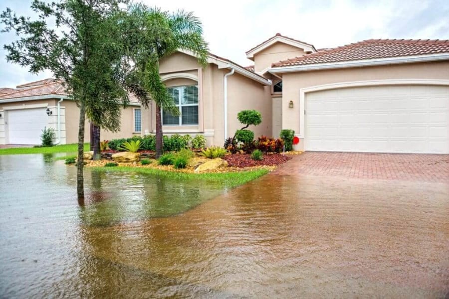 The front of a house with rising flood water in the front lawn and driveway.