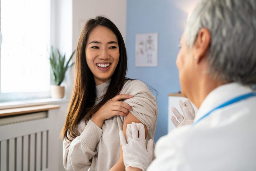 Senior Caucasian female doctor, giving an flu vaccine to a female patient Japanese ethnicity, during an annual medical check-up
