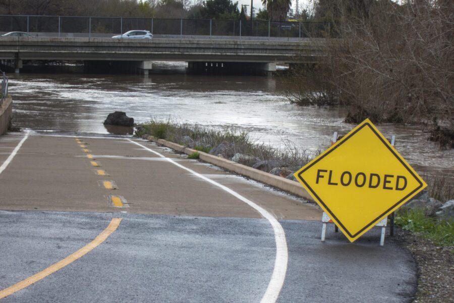 A flooded road with a yellow "flooded" sign in front of it