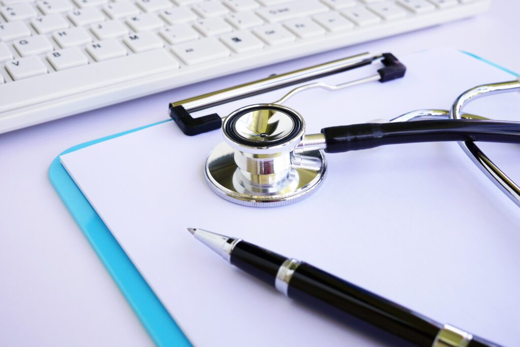 A stethoscope, clipboard and computer keyboard on a desk in a medical office setting
