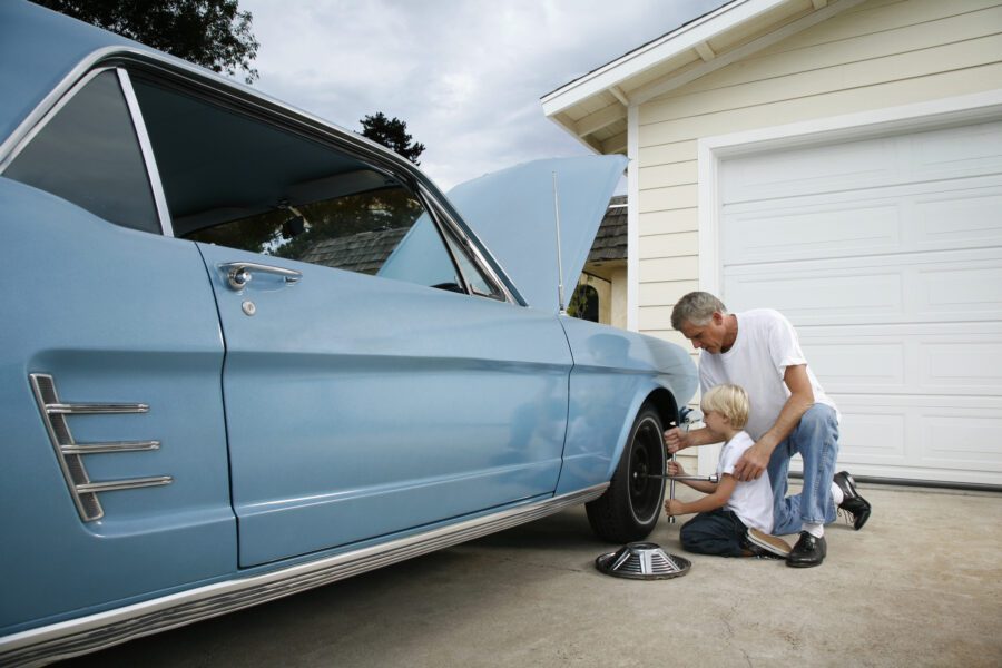 Father and son working together to fix a classic car in the driveway of their home