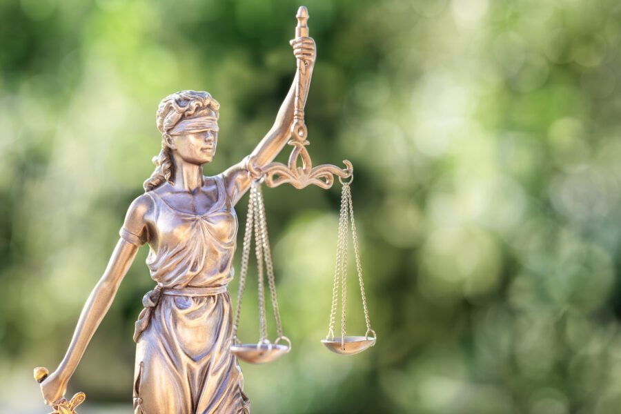 Bronze statue of Lady Justice holding balanced scales with a blurred green background