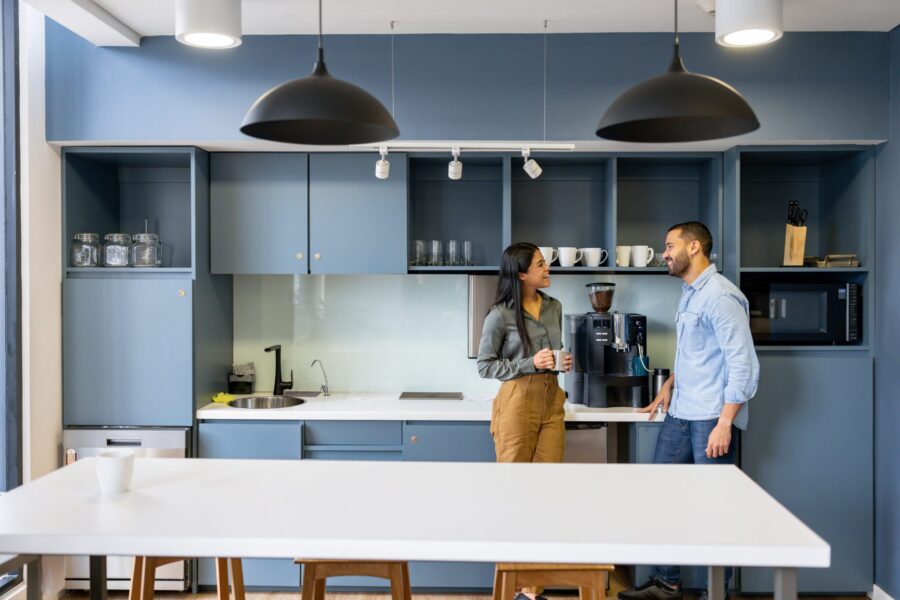 Happy coworkers talking in the breakroom area near a coffee pot while taking a break at the office