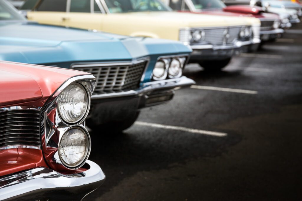 Classic auto vehicles in a row parked on asphalt parking lot participating in a classic car show