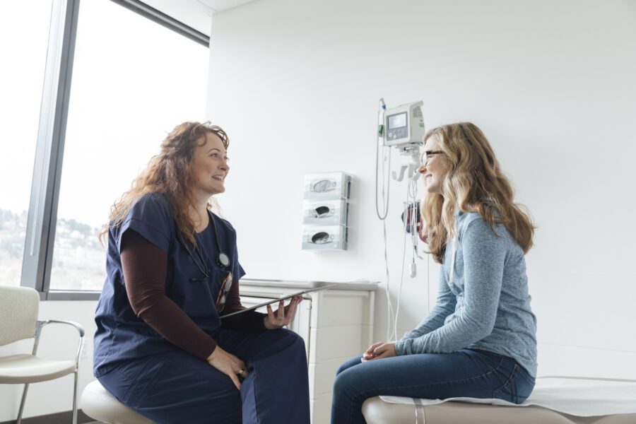 Smiling female nurse using digital tablet while talking to teenage patient in clinic