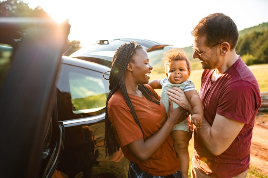 Adventurous Married Couple With Little Baby Standing Beside Their Car In Nature On A Sunny Day