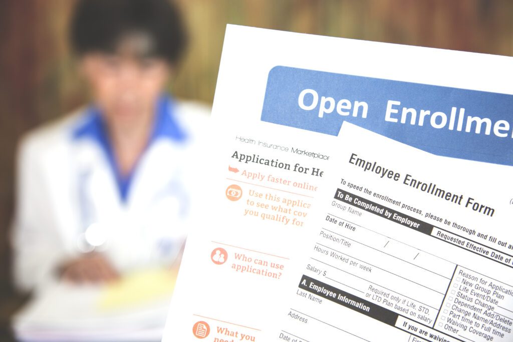 Patient holding open enrollment health care benefits forms with a medical doctor in the background