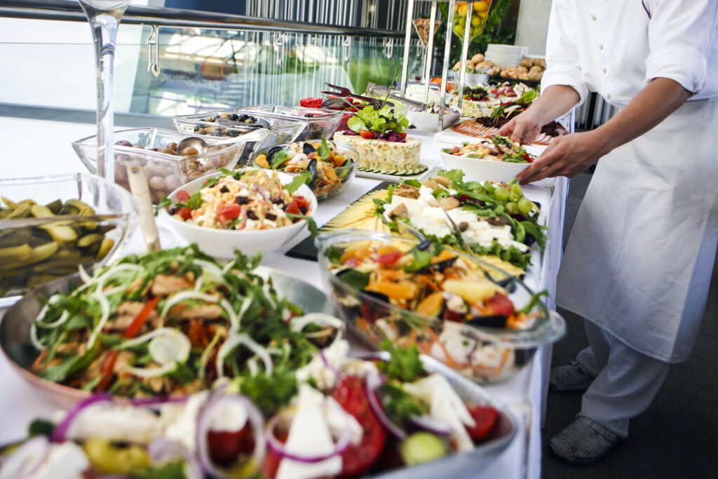 Professional waiter in white apron and uniform serving a large buffet table full of delicious food