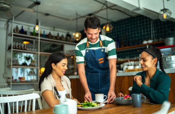 Cafe waiter serving coffee to two female patrons at a restaurant