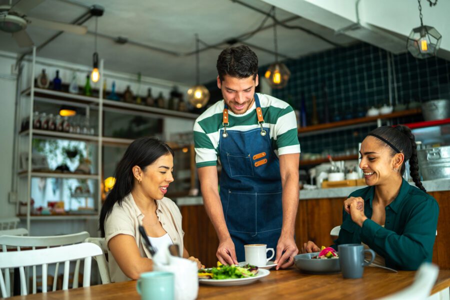 Cafe waiter serving coffee to two female patrons at a restaurant