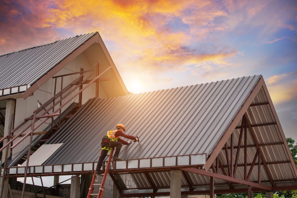Roofing contractor working installing metal sheet roofing on a building at sunset