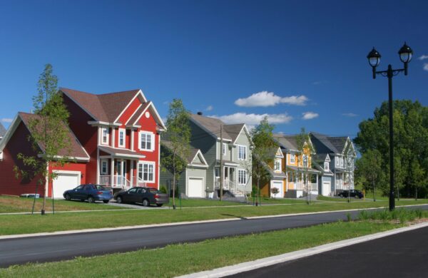 Four colorful suburban homes with grass front yards on a tree-lined street
