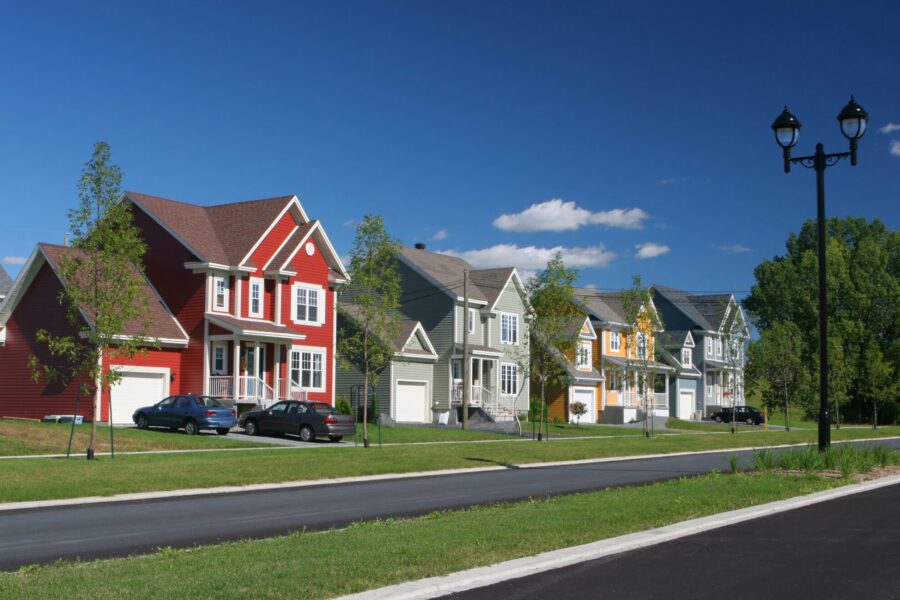 Four colorful suburban homes with grass front yards on a tree-lined street