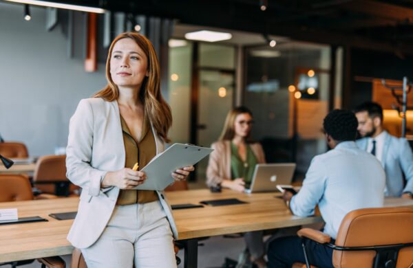 Business woman holding a clipboard with her colleagues in the background during a meeting in board room