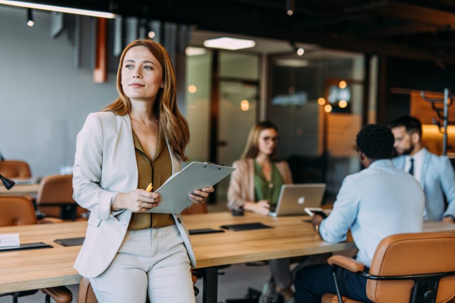Business woman holding a clipboard with her colleagues in the background during a meeting in board room