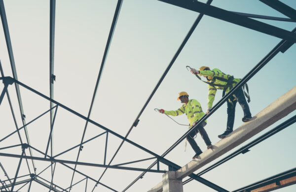 Two construction workers install a steel roof sheet for the new roof of a residential building that is under construction