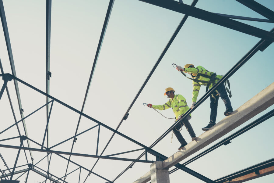 Two construction workers install a steel roof sheet for the new roof of a residential building that is under construction