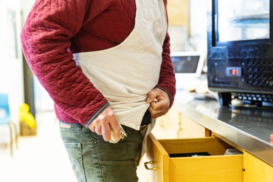 A male employee stealing money from a cash register till