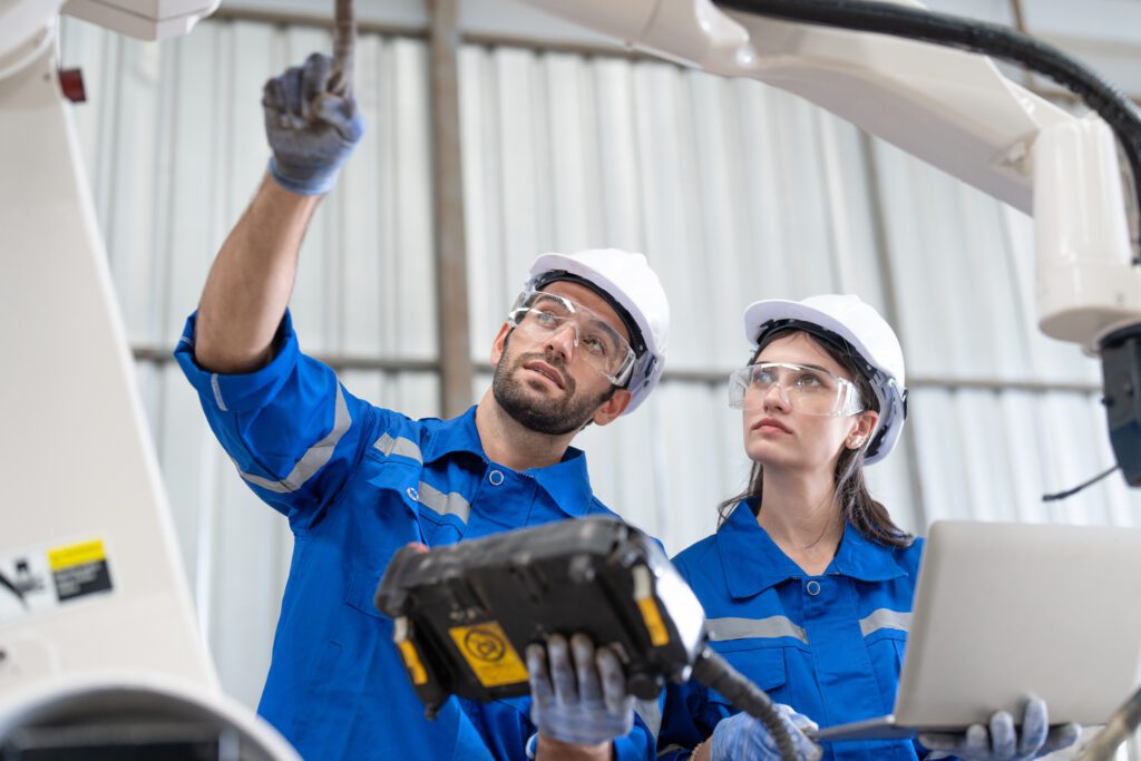 Male and female engineer examine a robot arm in a factory while investigating a workplace incident