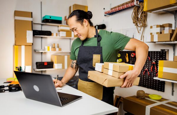 A small business owner wearing an apron takes inventory using a laptop computer