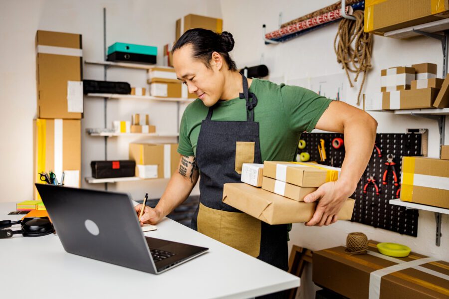 A small business owner wearing an apron takes inventory using a laptop computer