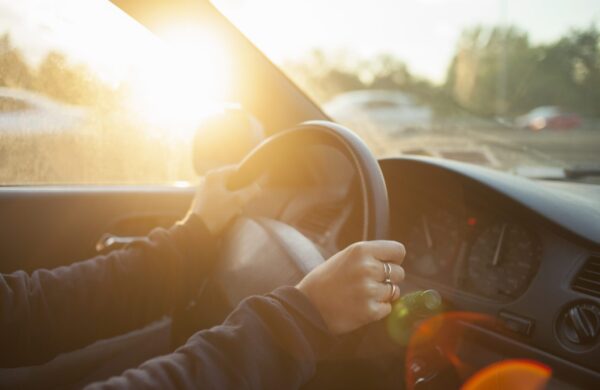 A person drives a car with sunlight streaming through the window, hands steady on the wheel and the dashboard gleaming