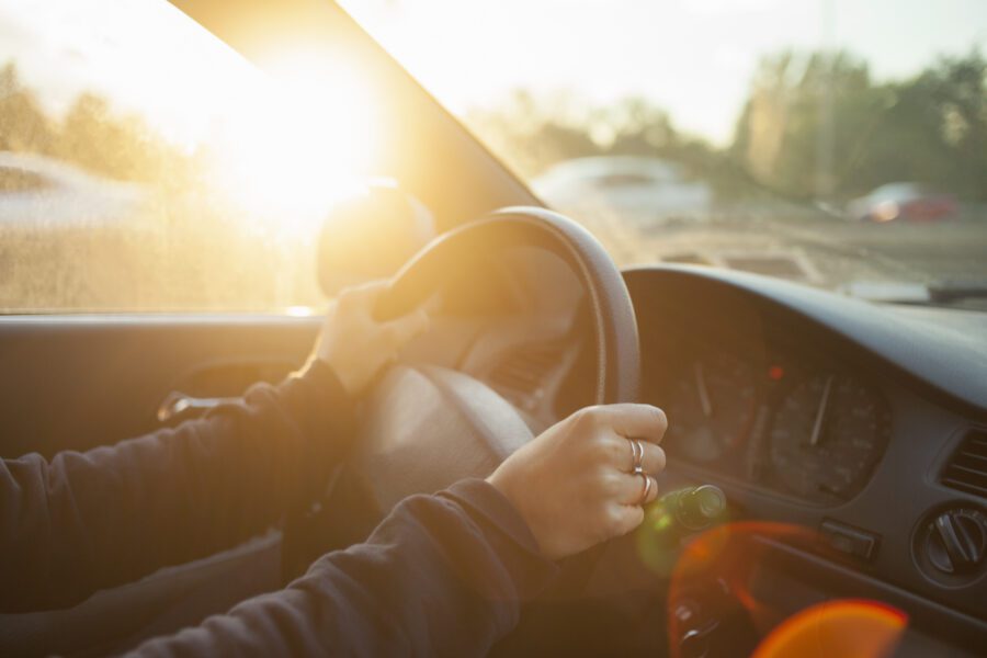 A person drives a car with sunlight streaming through the window, hands steady on the wheel and the dashboard gleaming