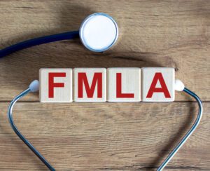 Wooden blocks spelling "FMLA" with a stethoscope on a wooden surface, highlighting the Family and Medical Leave Act in healthcare—relevant for the April 2025 HR Update.