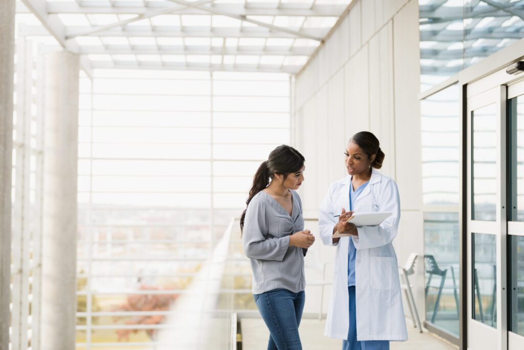 The mid adult female doctor explains the patient's test results to the young adult female family member as they stand in the hospital walkway