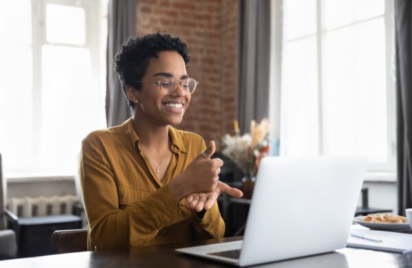 Smiling therapist in glasses talking on a video call, using sign language to speak to a patient with a hearing disability