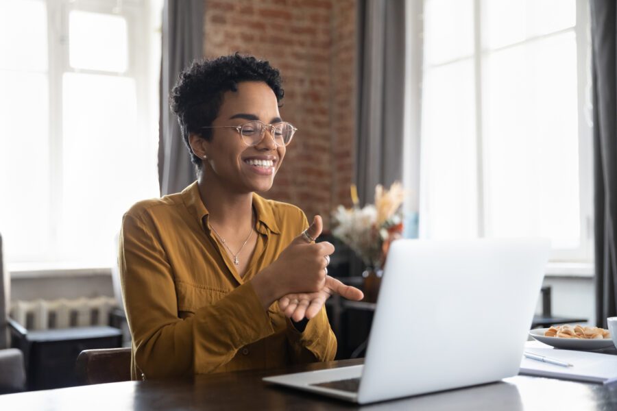 Smiling therapist in glasses talking on a video call, using sign language to speak to a patient with a hearing disability