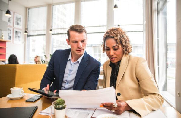 Two professionals looking at paperwork during a business discussion in a cafeteria-style restaurant