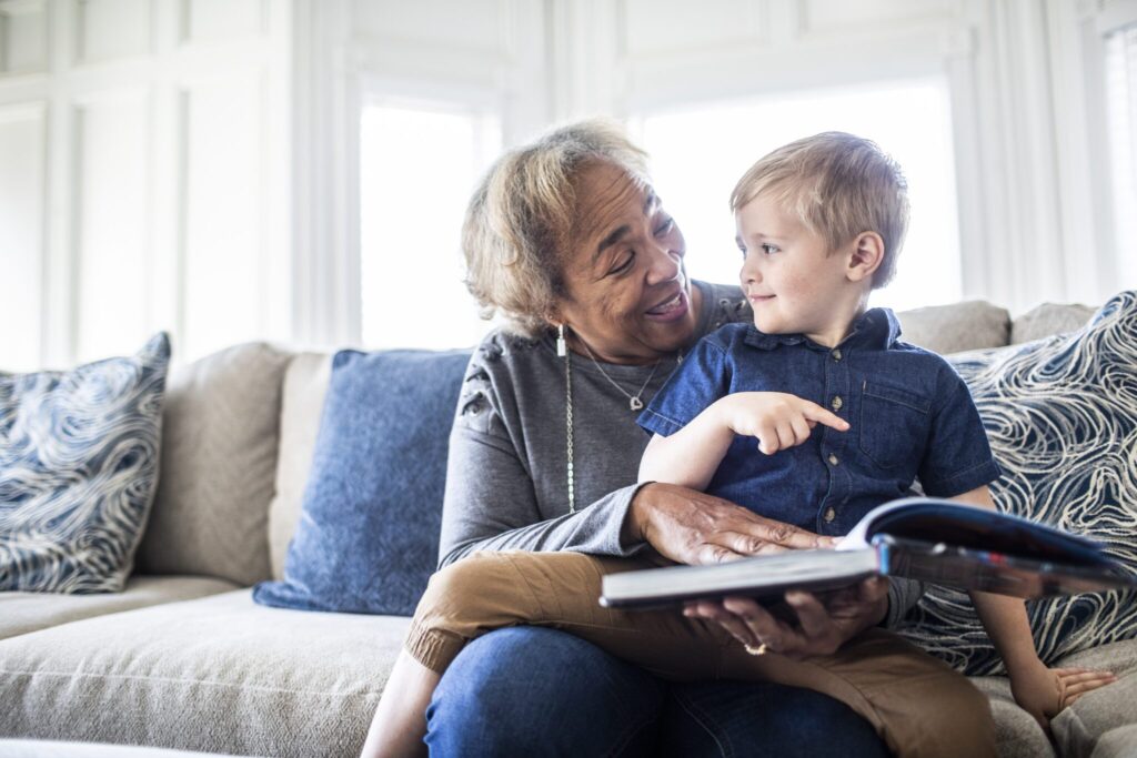 Grandmother reading a book with her toddler grandson while sitting on a couch