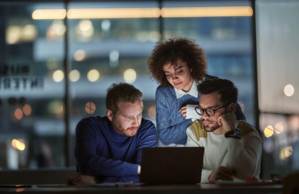 Group of young entrepreneurs cooperating while reading an e-mail on laptop late in the office