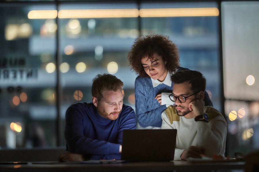 Group of young entrepreneurs cooperating while reading an e-mail on laptop late in the office