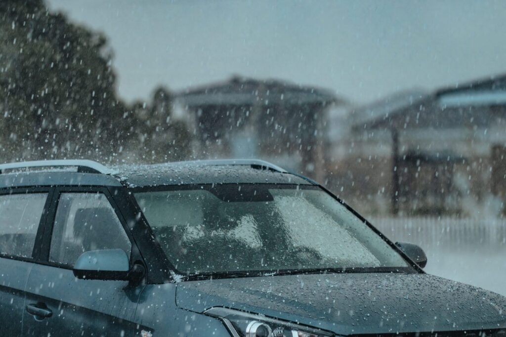 A car parked and being damaged by rain and a hailstorm