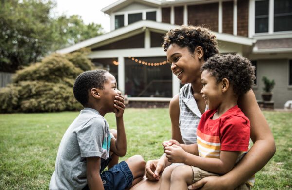 Single mother playing with young sons in front of house