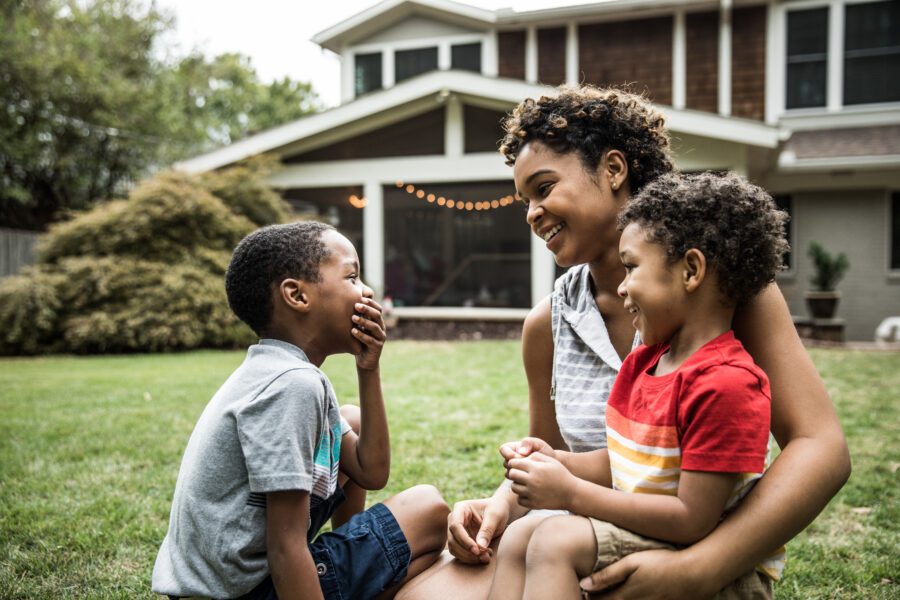 Single mother playing with young sons in front of house