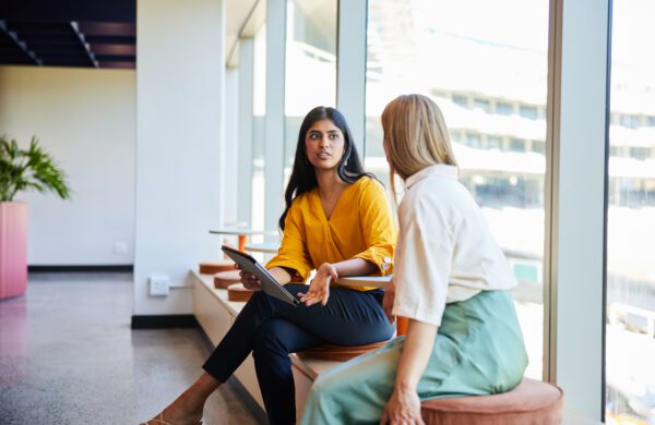 Young businesswoman discussing work on a digital tablet with a female colleague at a table in the hallway of a modern office