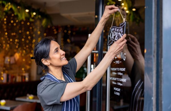 Happy female small business owner hanging an open sign on the storefront door